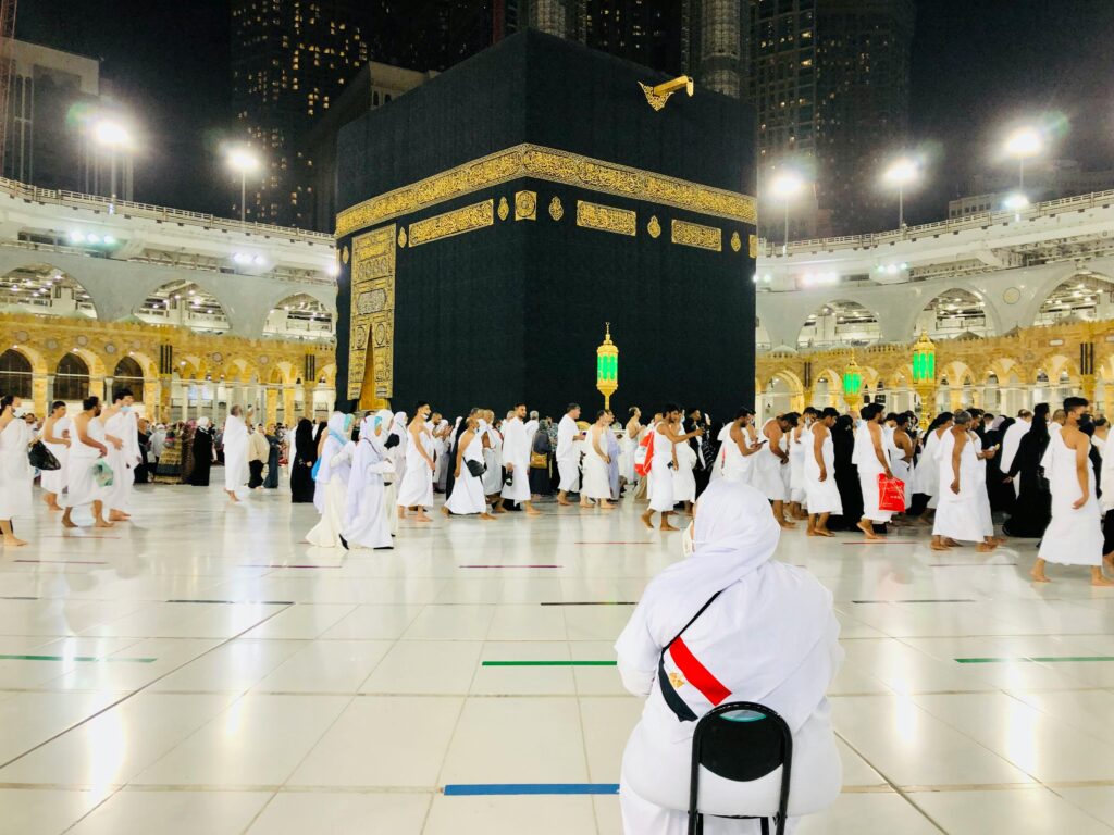 Muslim pilgrims perform Tawaf around the Kaaba in Mecca under bright lights at night.